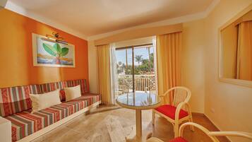 Una habitación con sofá, una mesa redonda y una silla. Hay una ventana con cortinas y un cuadro en la pared.