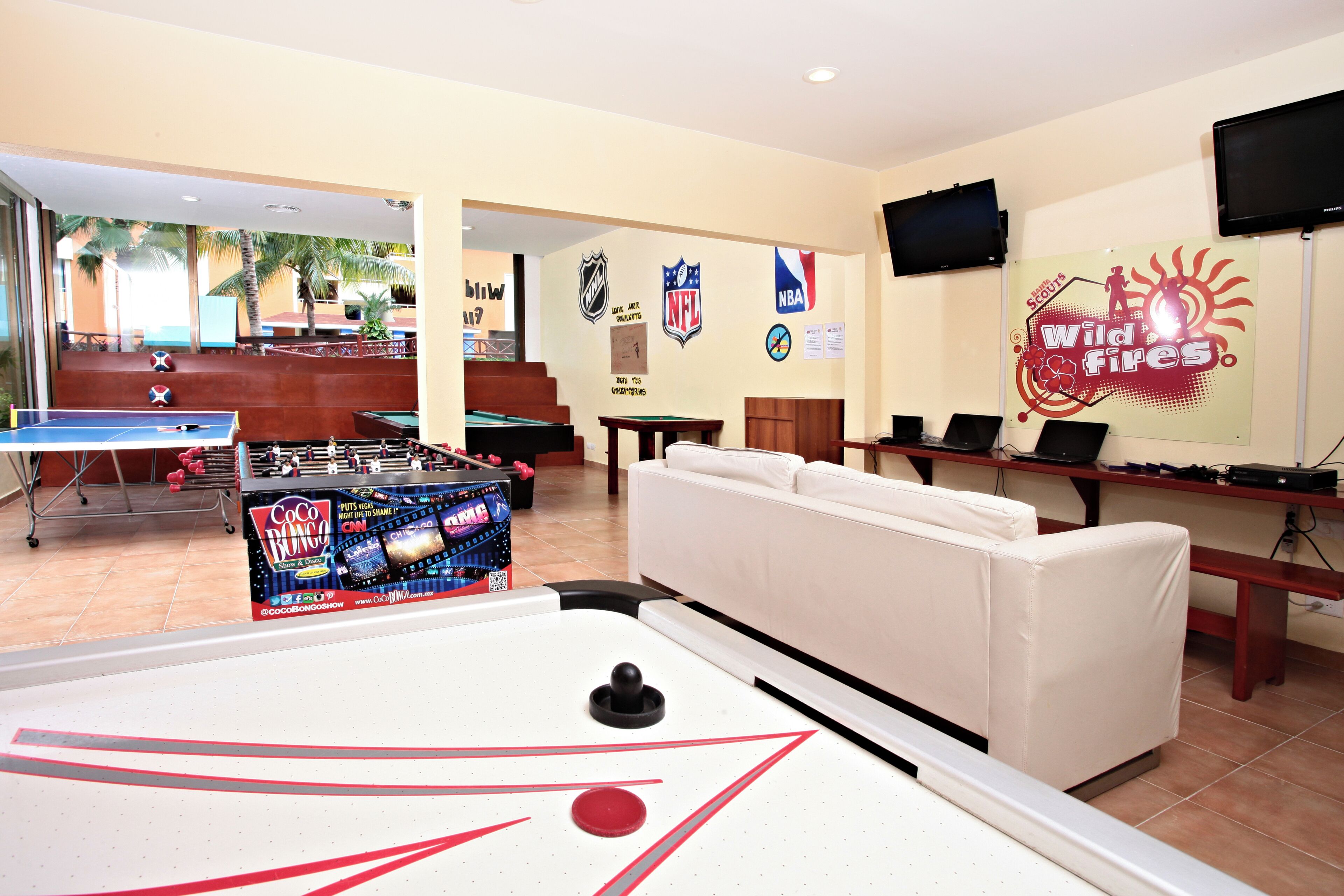 Une table de billard, une table de baby-foot, un canapé et un mur orné de logos d’équipes sportives.