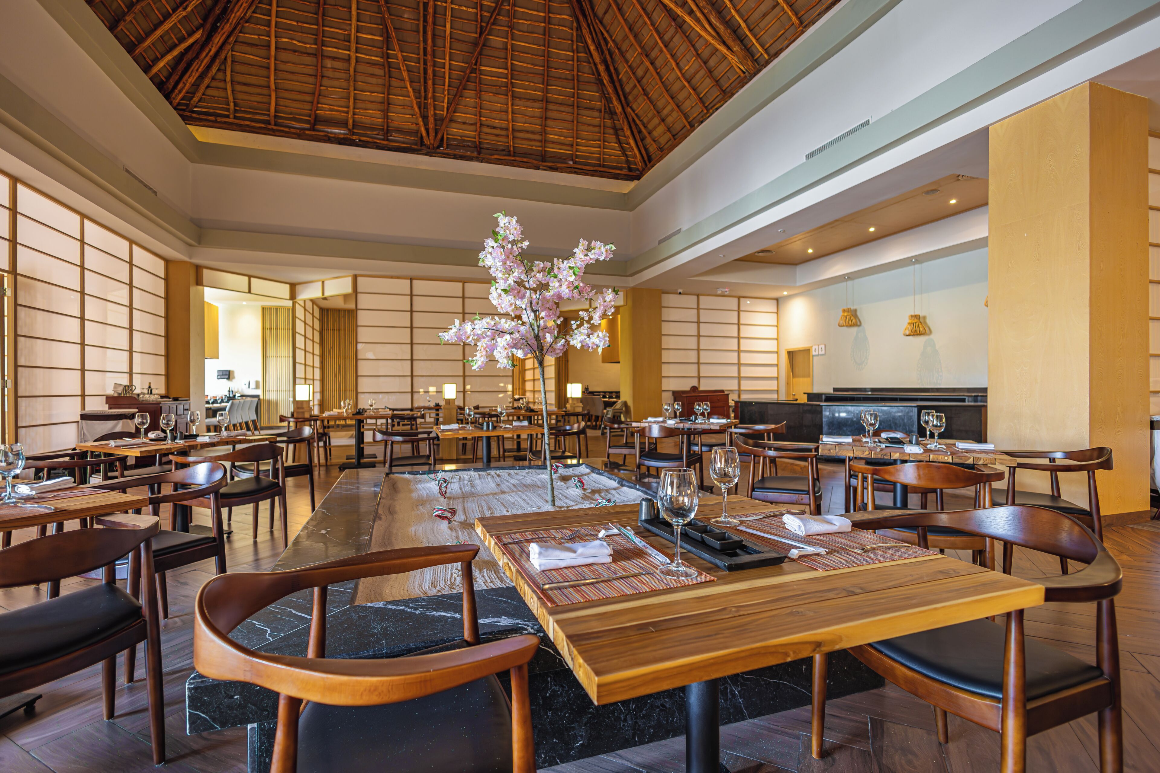 A spacious restaurant with wooden tables and chairs, a central floral arrangement, and a traditional bamboo ceiling.