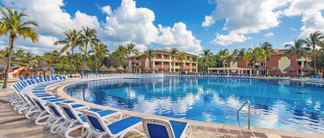 A swimming pool with lounge chairs, palm trees, and a building with a red and beige facade.