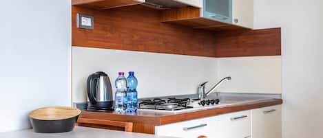 A compact kitchen with a wooden countertop, a gas stove, a kettle, and a sink. There are two bottles of water and a bowl on the counter.