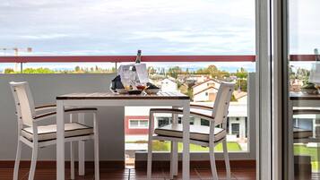 Un balcon avec une table dressée pour deux personnes, des chaises, une bouteille de champagne et une vue sur un quartier résidentiel.