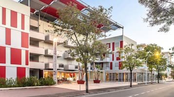 A modern hotel building with a red and white facade, multiple balconies, and potted plants in the foreground.