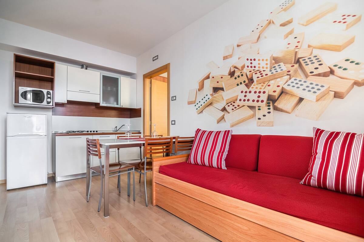 A compact living space with a kitchenette, a dining area, and a sofa with red cushions.