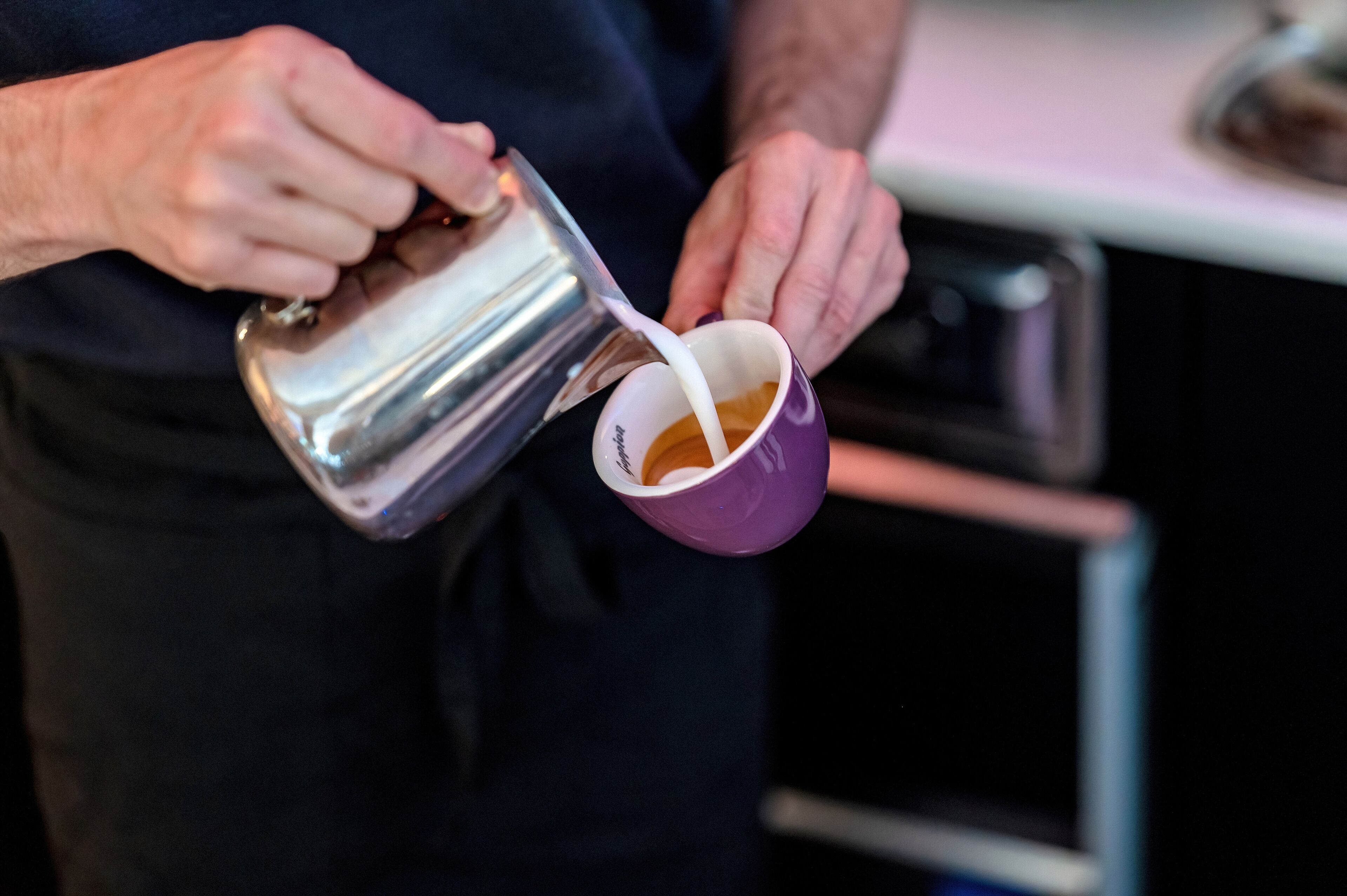 Una persona versa un liquido da un boccale di metallo in una tazza viola.