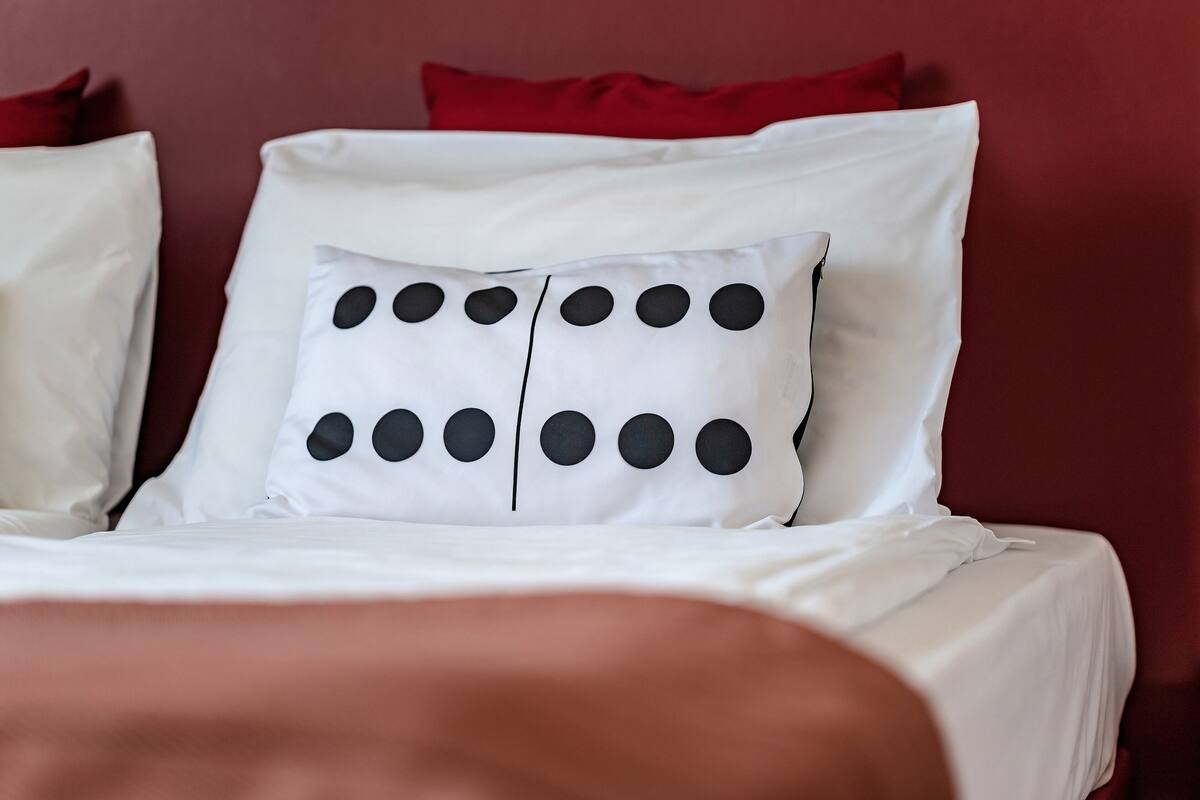 A bed with white bedding and a pillow featuring black circular patterns.