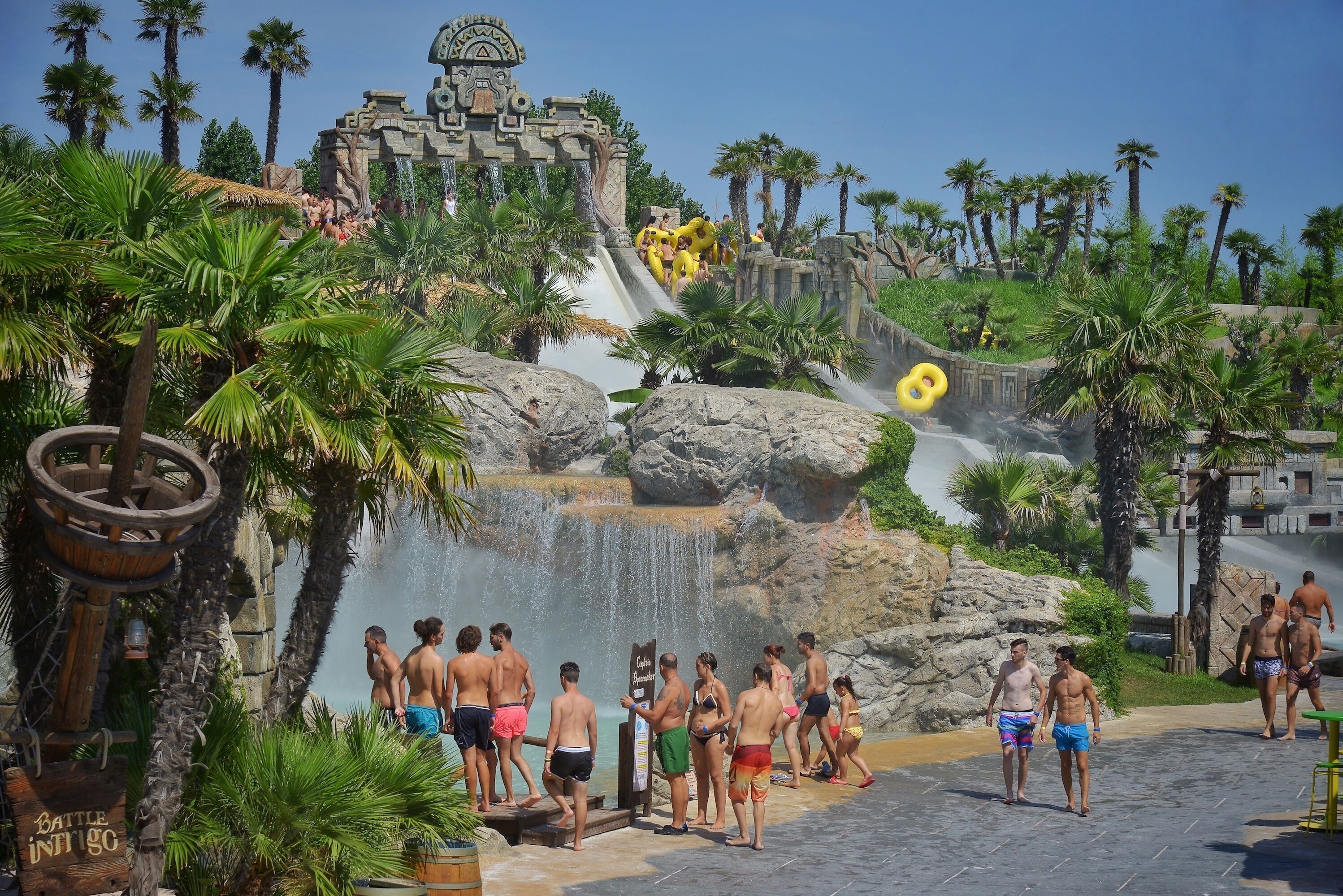 Un parc aquatique doté d’une cascade, de palmiers et d’une structure en pierre en arrière-plan.
