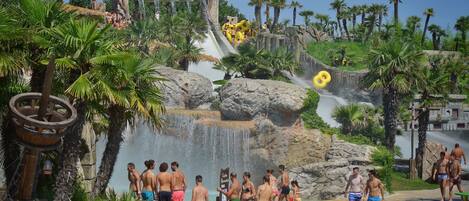 A water park with a waterfall attraction, palm trees, and a stone structure in the background.