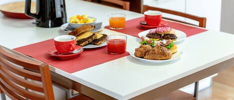 A breakfast table with a coffee pot, fruit bowl, juice, and pastries.