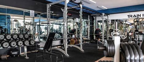 A gym with weightlifting equipment, mirrors, and a 'TRAIN IN' sign.
