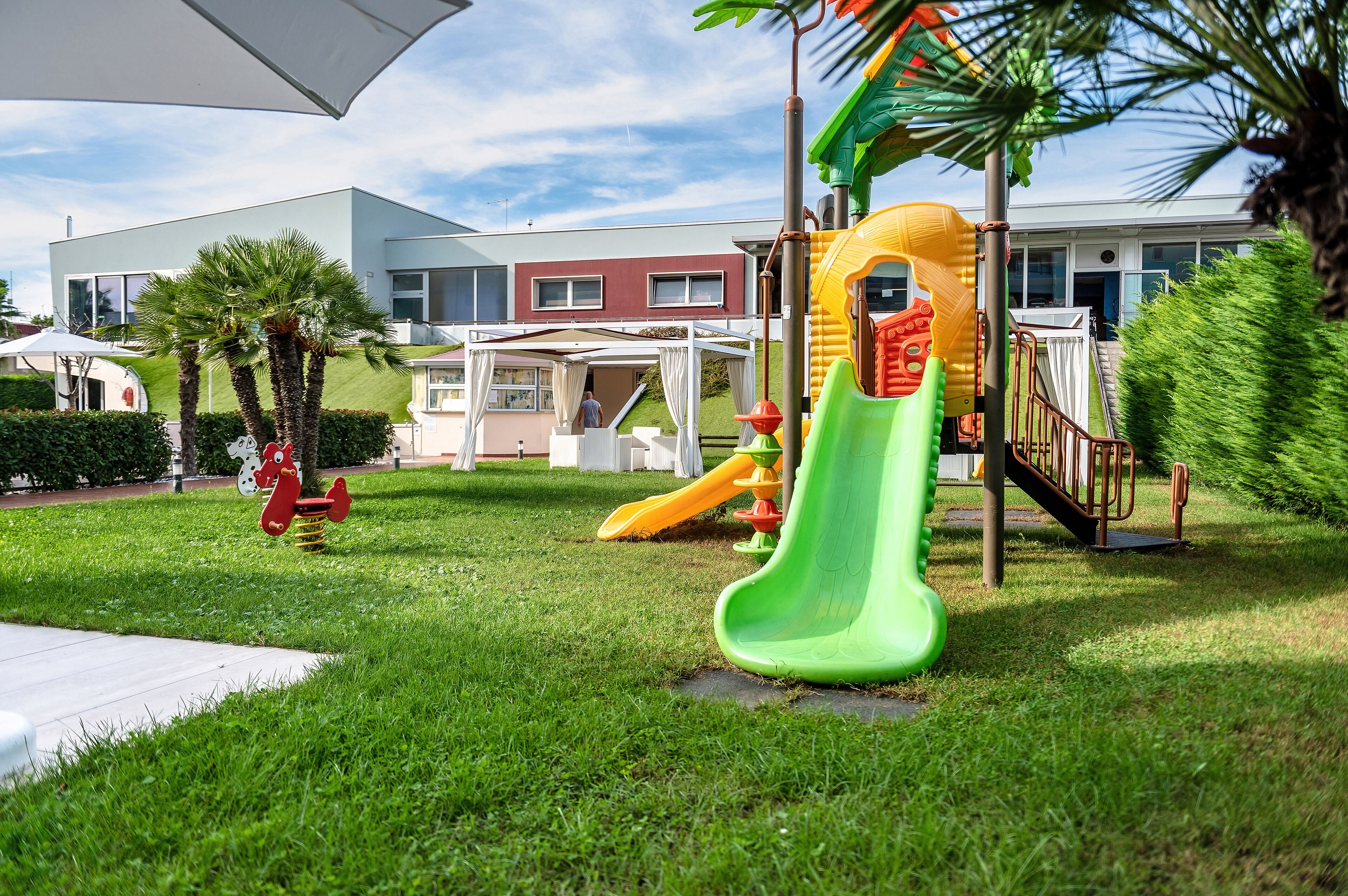 A playground with slides and swings, surrounded by a well-maintained lawn and palm trees.
