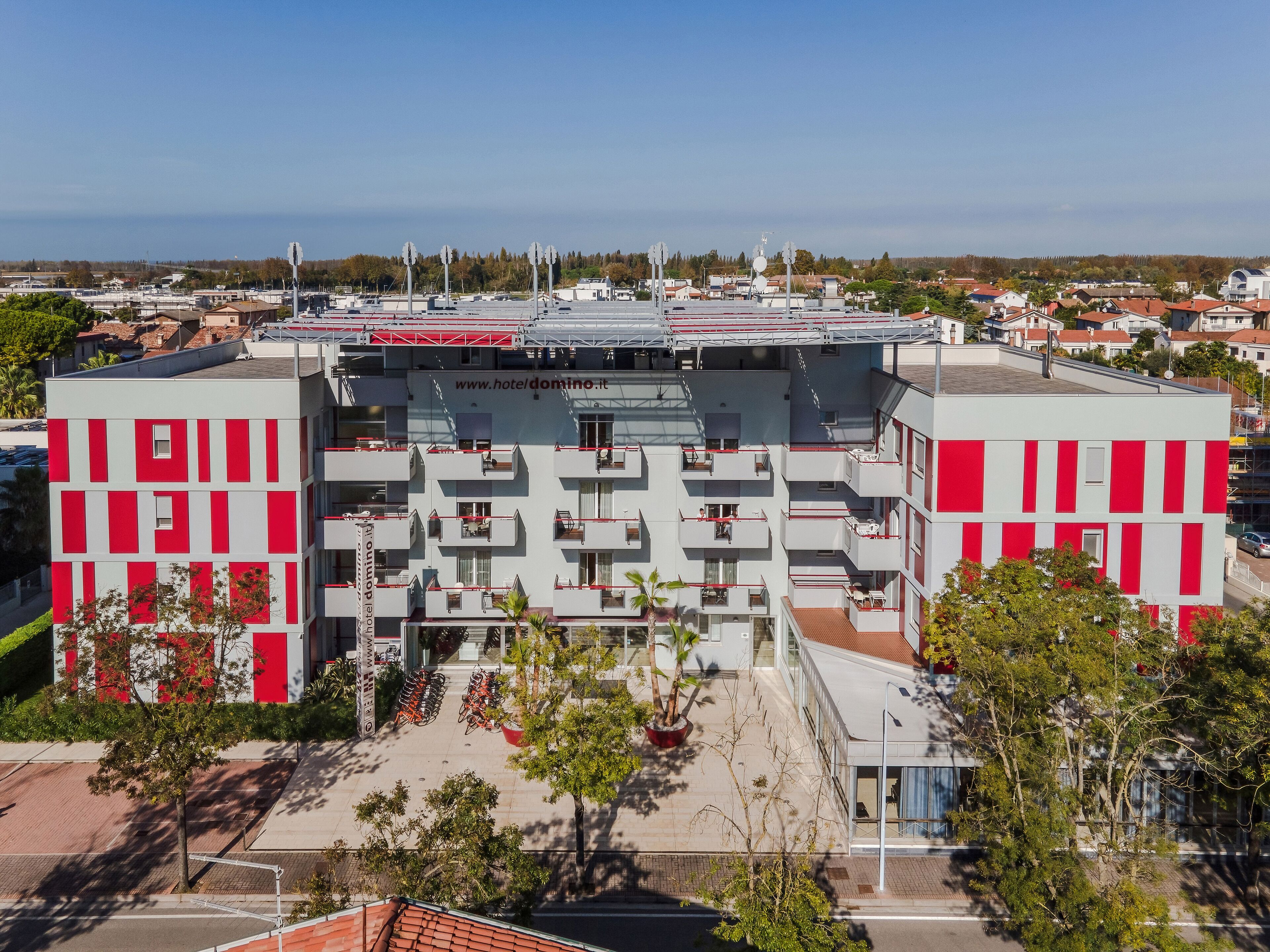 A multi-story hotel with a red and white facade, balconies, and a rooftop terrace.