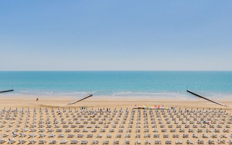 A beach with rows of sun loungers and umbrellas, a pier, and calm blue waters.