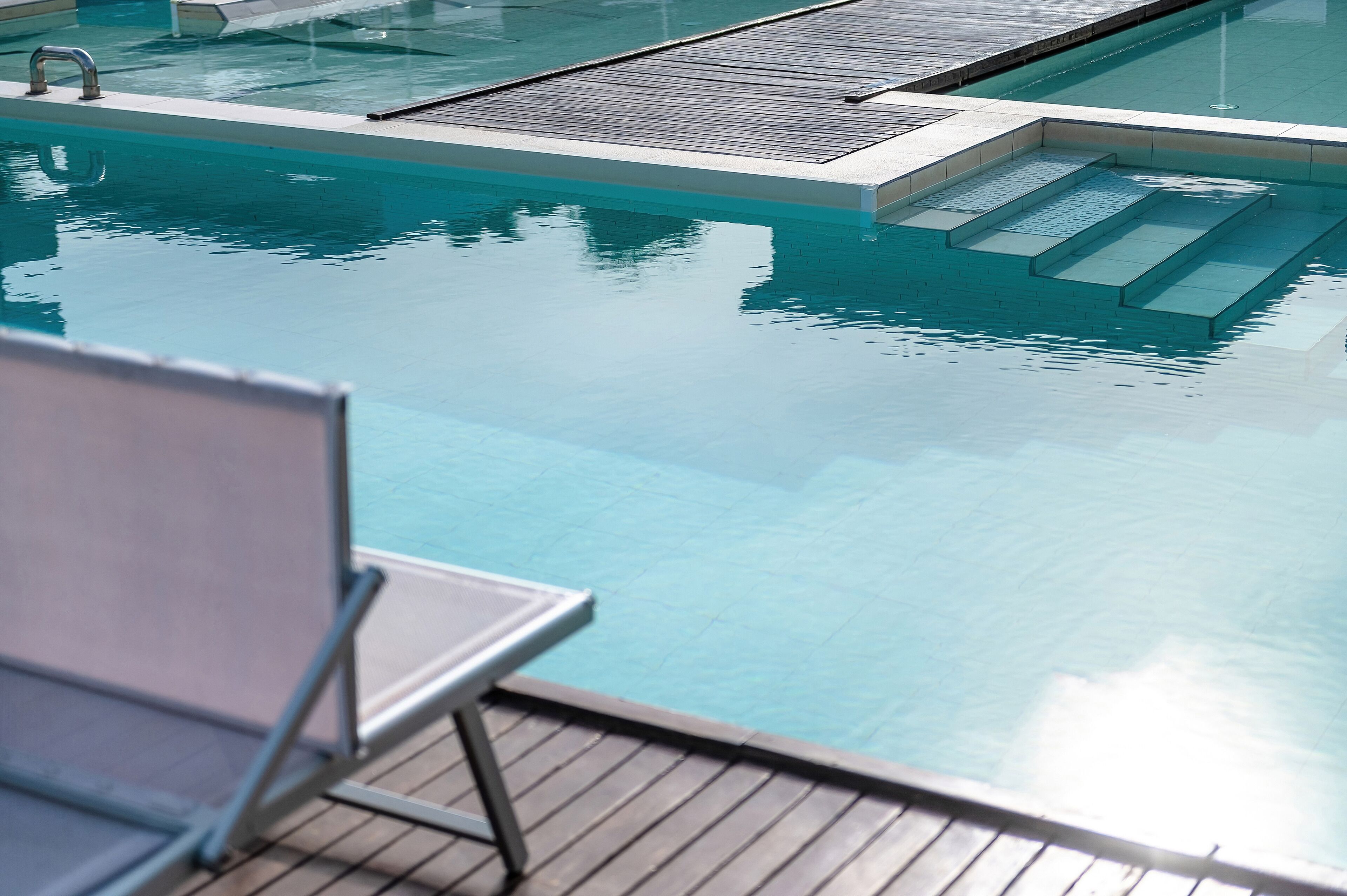 Una piscina con agua cristalina, cubierta de madera y una silla de metal.