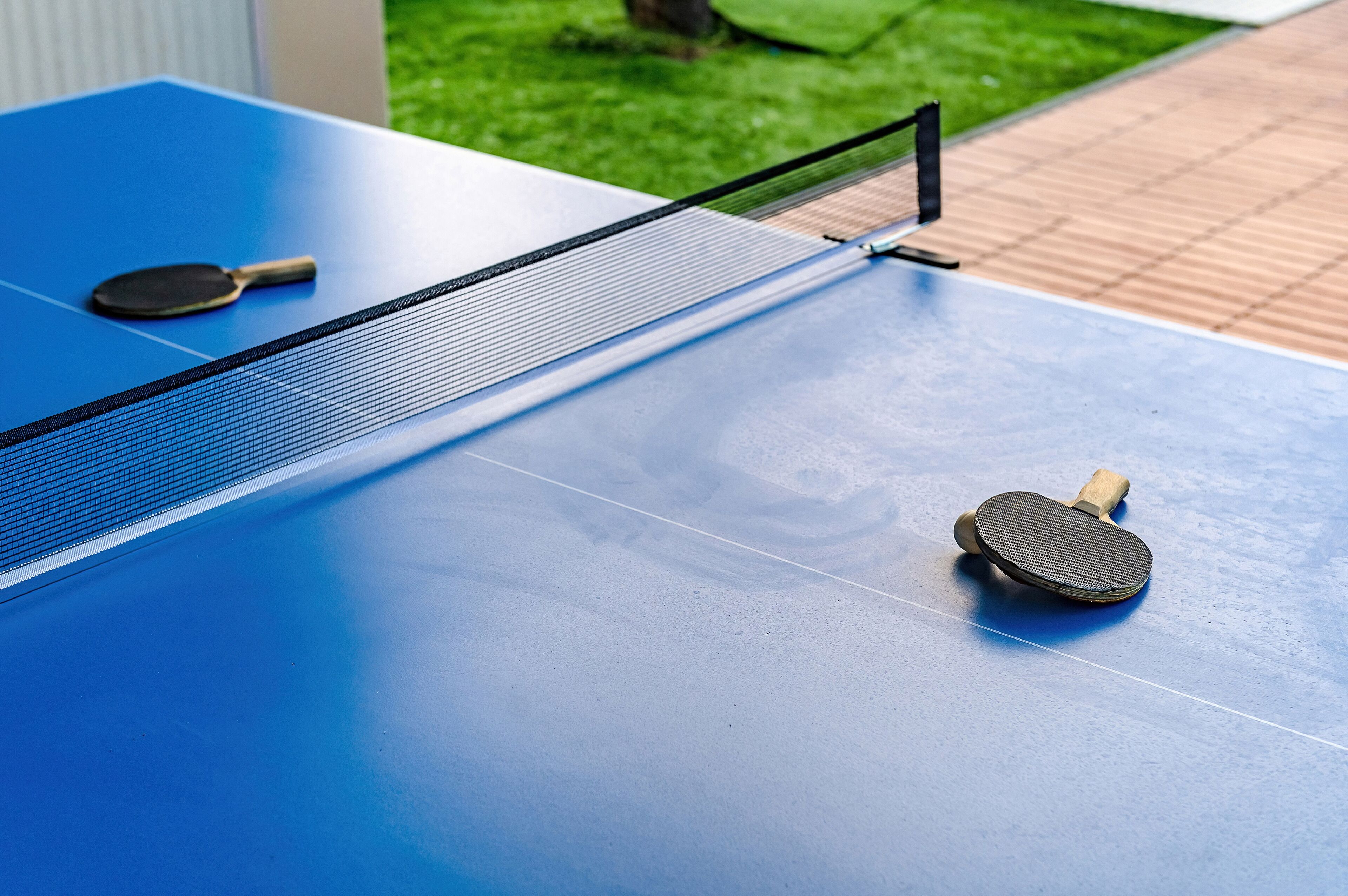 Une table de ping-pong bleue, avec un filet et deux raquettes.