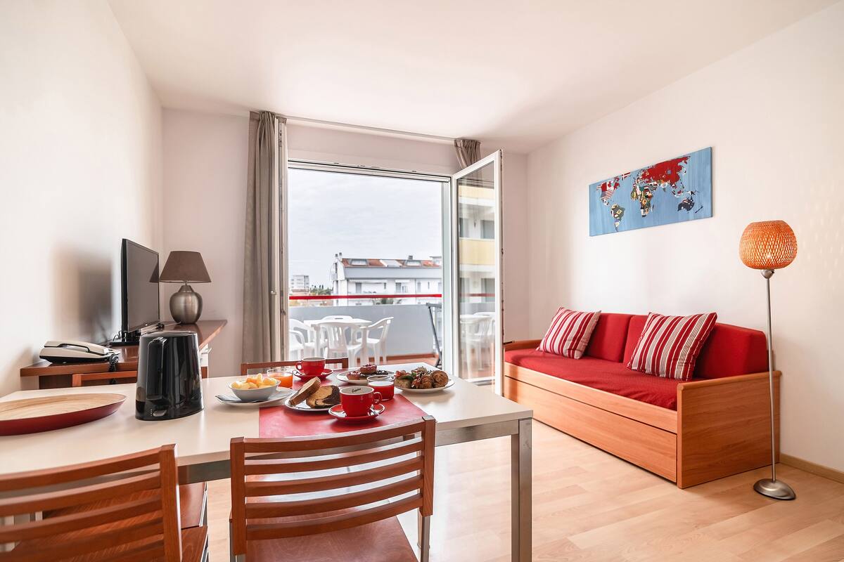 A modern living room with a red sofa, a dining table with chairs, a TV, and a world map artwork.
