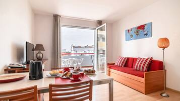 Ein modernes Wohnzimmer mit einem roten Sofa, einem Esstisch mit Stühlen, einem Fernseher und einem Wandbild einer Weltkarte.