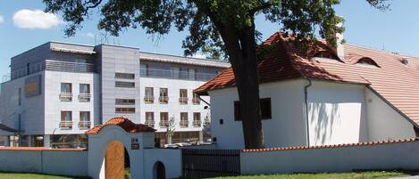 A building with a modern facade, a traditional building with a red-tiled roof, and a large tree in front.