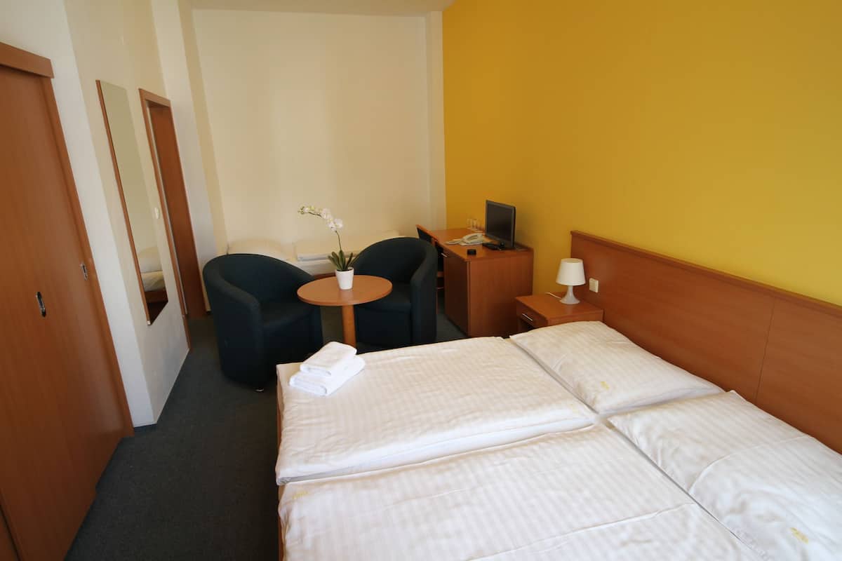Ett hotellrum med en säng, ett skrivbord med en dator, en stol, ett litet bord med en växt och en spegel.