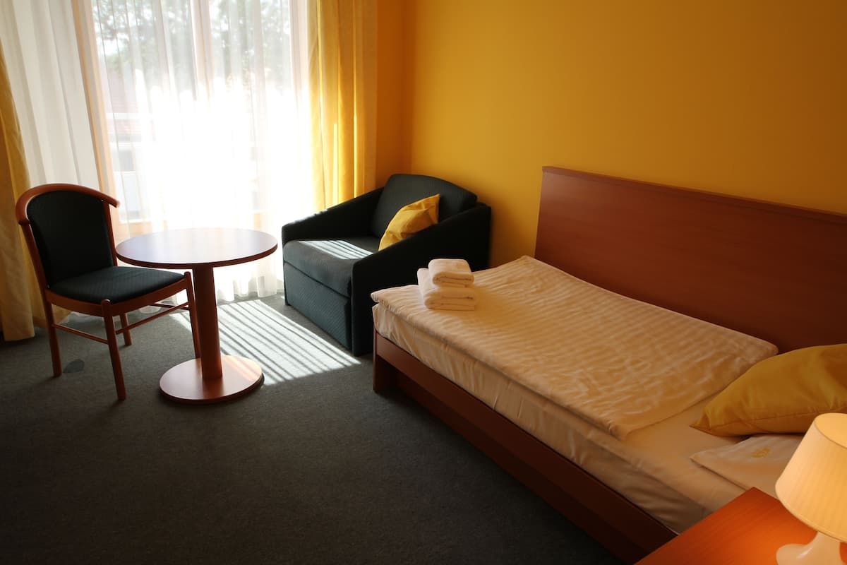 Ett hotellrum med en säng, en stol, ett litet bord och en lampa.