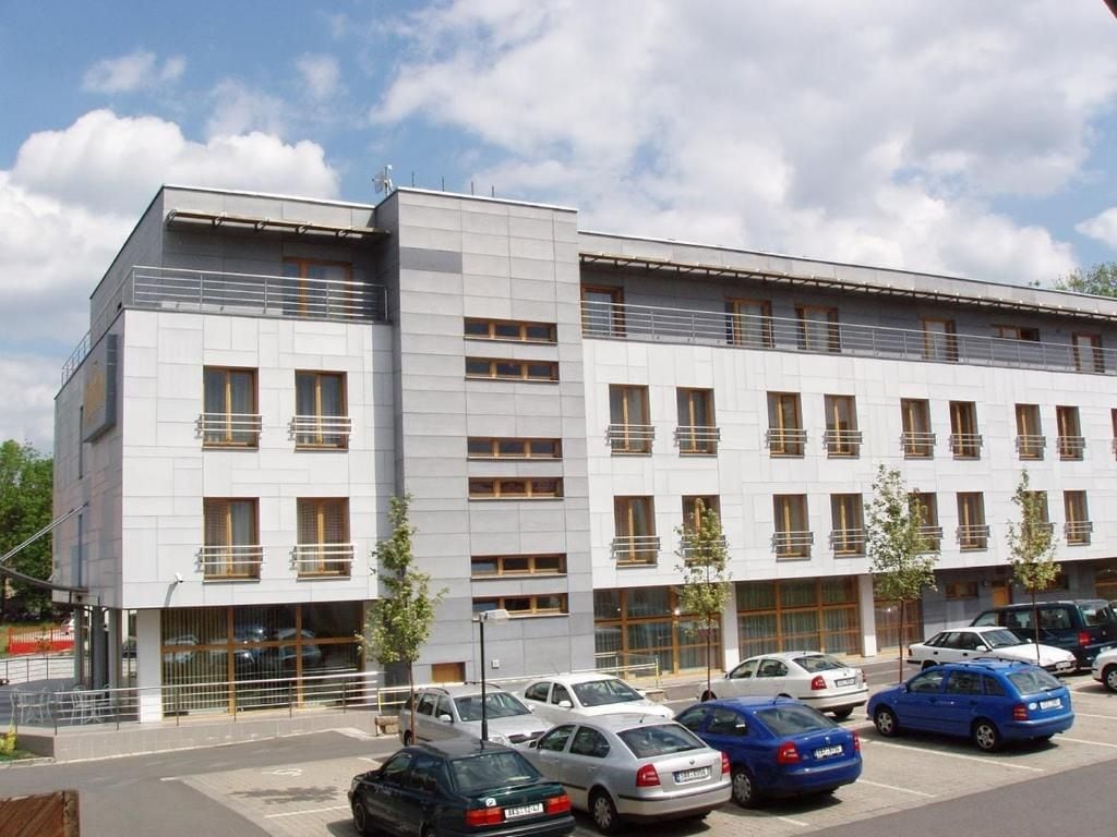 A modern building with multiple floors, a parking lot with several cars, and a clear sky.