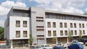 A modern building with multiple floors, a parking lot with several cars, and a clear sky.