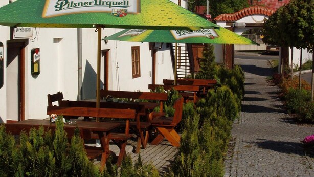 Ein Restaurant mit Außenbereich und einer grünen Markise mit der Aufschrift 'Pilsner Urquell'.