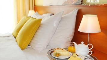 Una habitación de hotel con una cama, almohadas, una bandeja con alimentos para el desayuno y una lámpara.