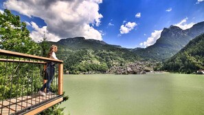A wooden bridge over a lake with a village in the background and mountains. - Hotel La Maison Wellness & SPA (Alleghe)
