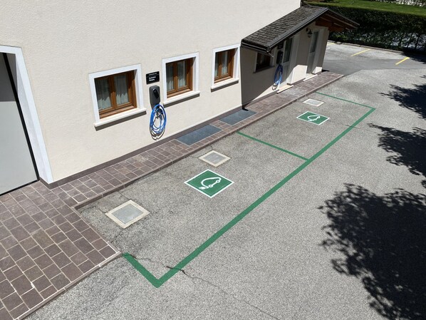 Un edificio con zona de estacionamiento para discapacitados, acceso cubierto y estación de carga para vehículos eléctricos azules.