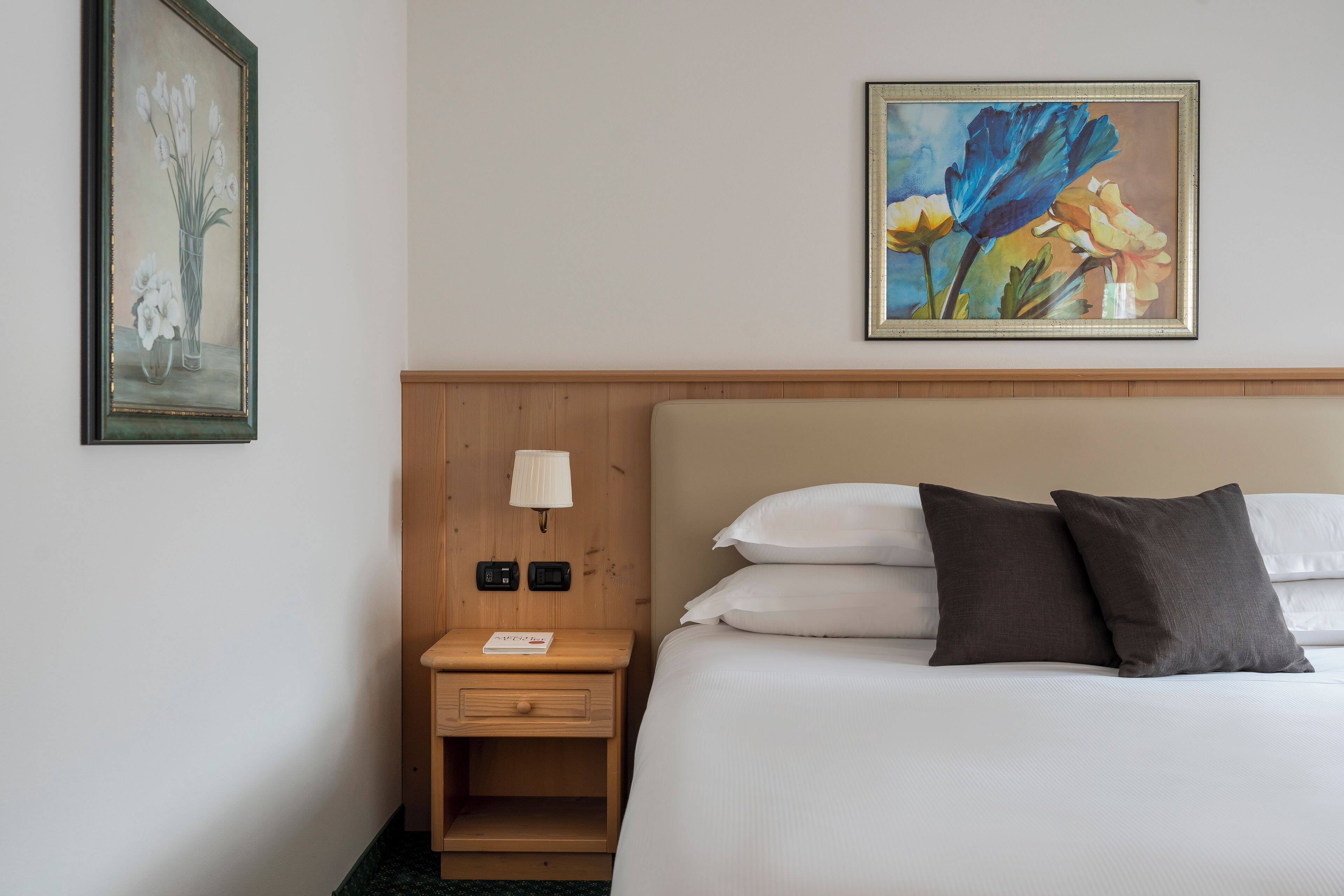 Une chambre d’hôtel avec un lit, une table de chevet avec une lampe et deux tableaux au mur.