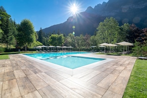 Una piscina rectangular con cubierta de madera, rodeada de abundante vegetación y montañas al fondo.