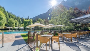 An outdoor patio with tables and chairs, a pool, and a mountainous backdrop. - Hotel La Maison Wellness & SPA (Alleghe)