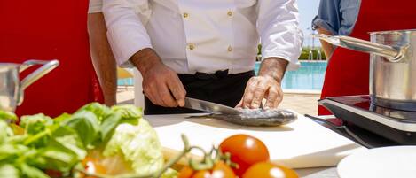 A chef preparing food outdoors with a cutting board, tomatoes, and a pot.