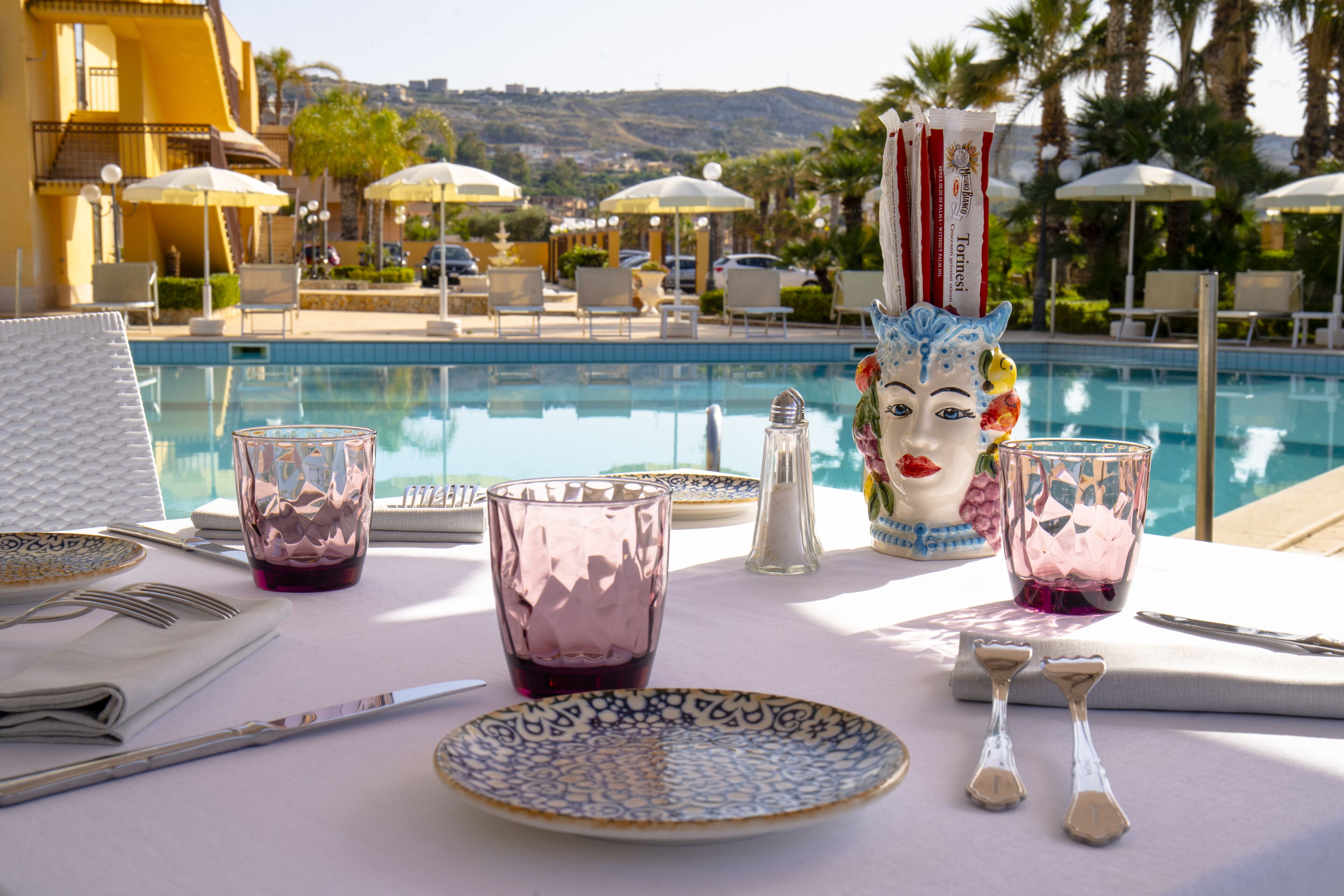 A poolside dining setup with a table, chairs, and a decorative mask.