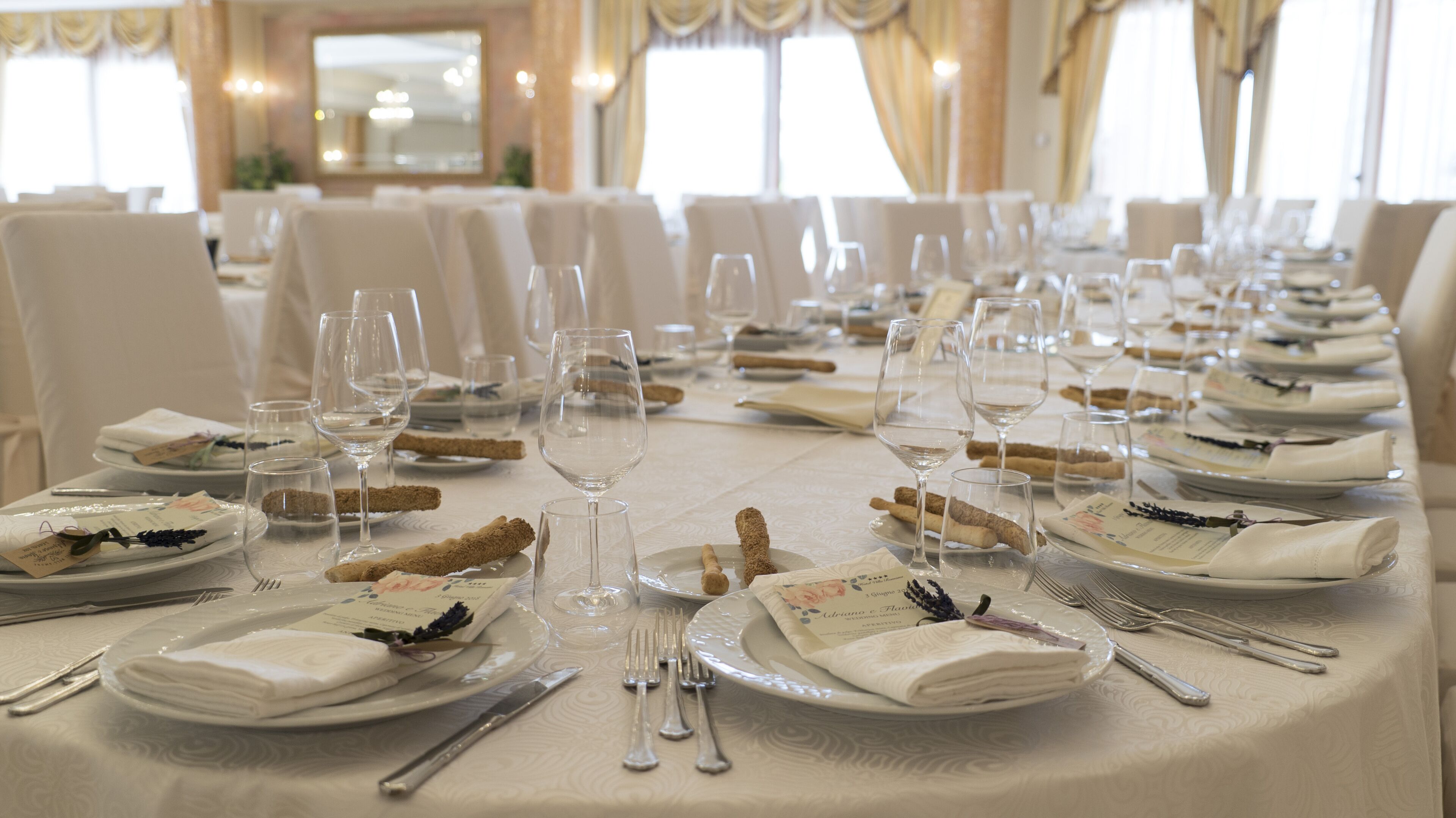A formal dining table set with white tablecloths, wine glasses, plates, and cutlery.