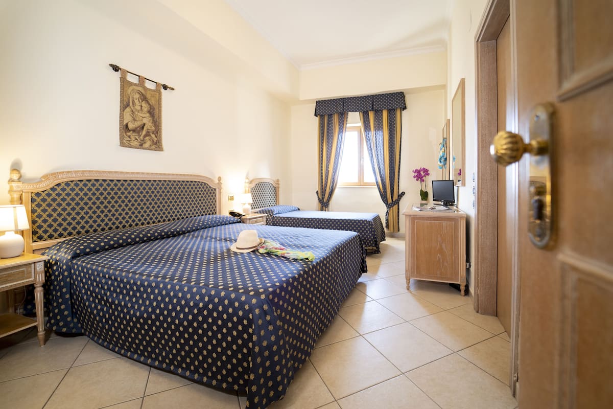 Une chambre d’hôtel avec deux lits, une commode en bois, un téléviseur et une fenêtre avec des rideaux.