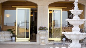 A multi-tiered fountain in front of a building with large glass doors and columns.