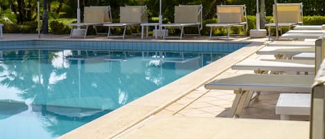Zona de piscina con sillas de descanso y sombrillas.