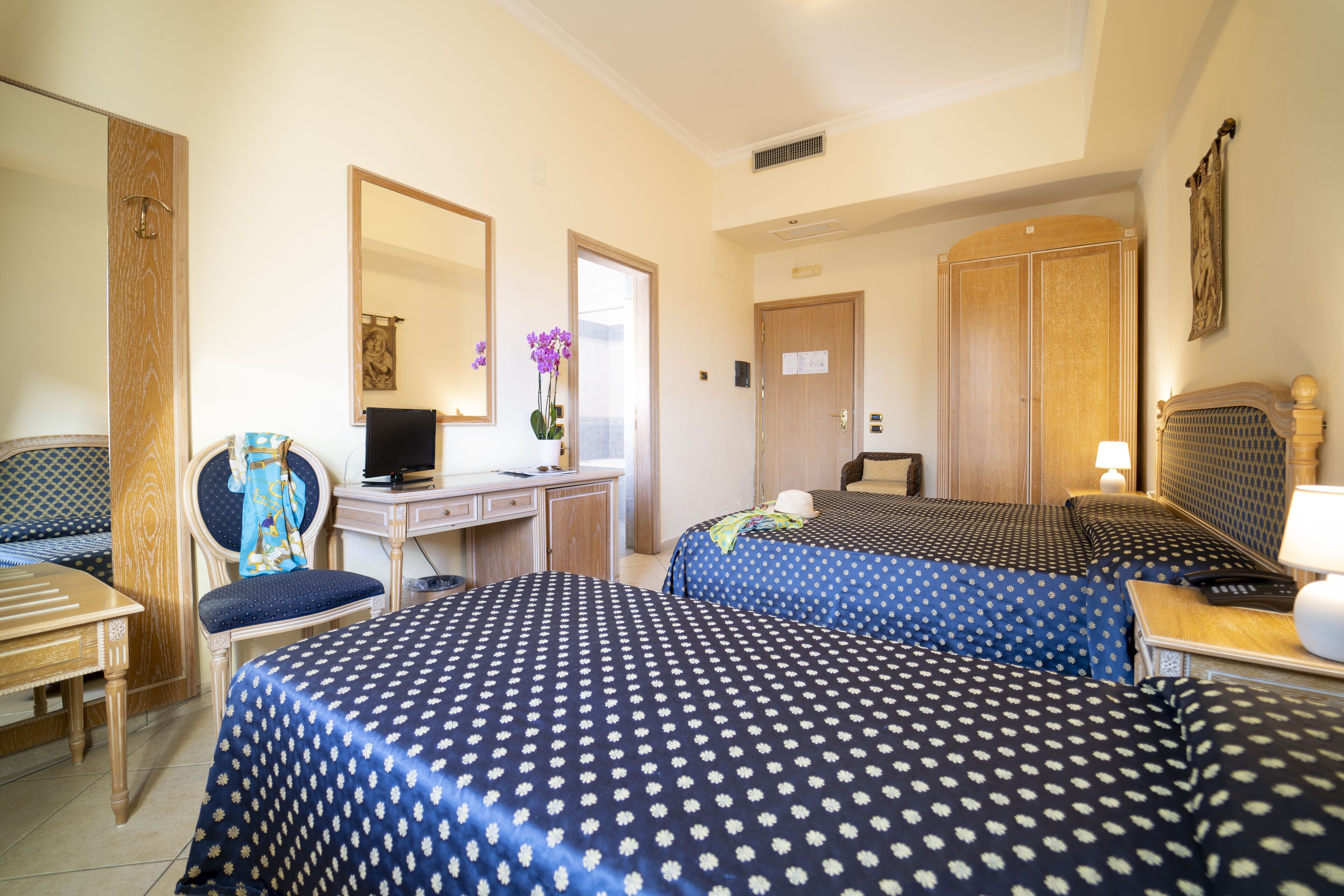 A hotel room with two beds, a desk with a computer, a chair, and a wardrobe.