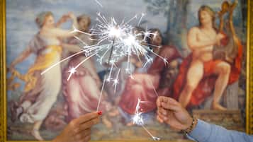 A painting with classical figures and a sparkler in the foreground.