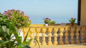 A balcony with a yellow balustrade, potted plants, and a view of the sea.