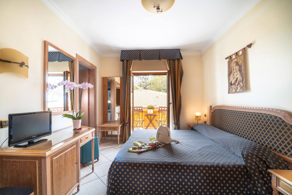 Une chambre d’hôtel équipée d’un lit, d’une télévision, d’un bureau, d’une chaise, d’un balcon et d’une fenêtre.