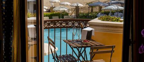 Zona junto a la piscina con mesa y sillas de madera, una botella de champán y sombrillas.