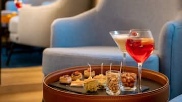 Uma bandeja com petiscos variados e um copo de martini sobre uma mesa em área de estar moderna, com sofás azuis.