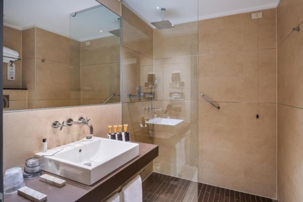 A modern bathroom with a large mirror, a white sink, and a glass shower enclosure.