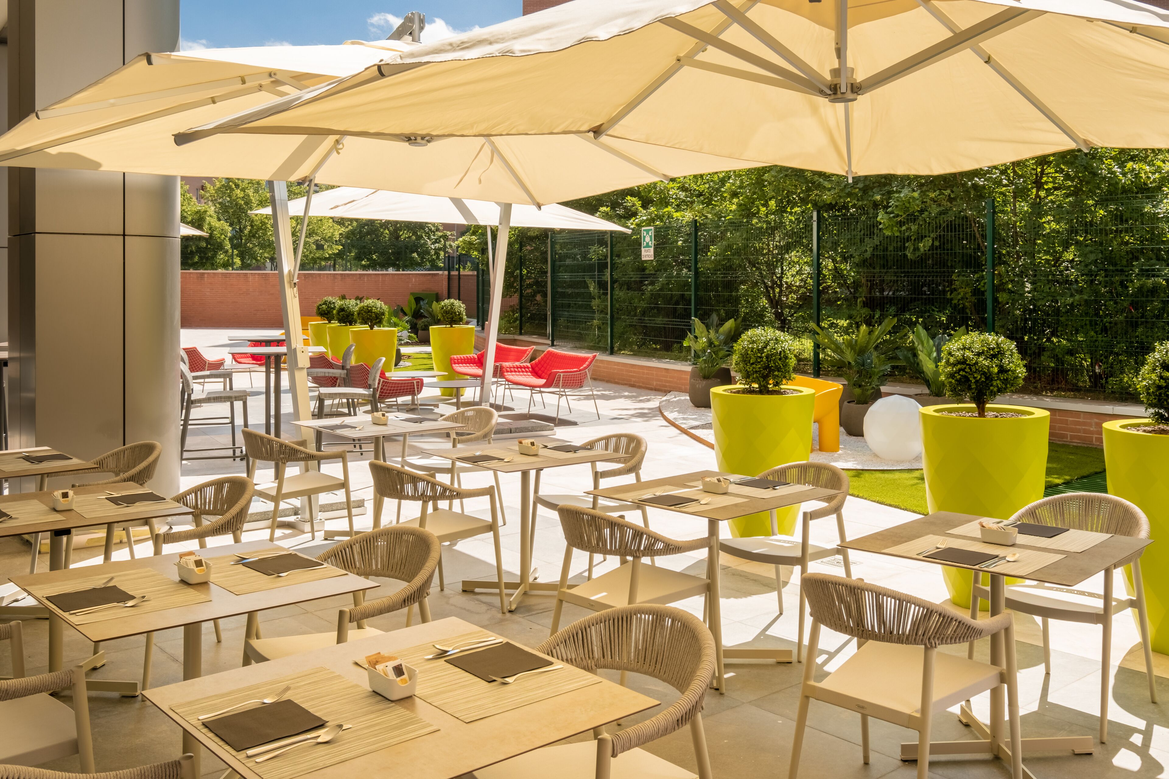 An outdoor cafe area with tables and chairs, umbrellas, and potted plants.