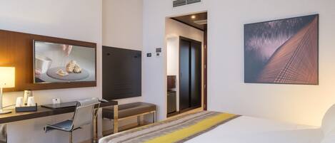 Habitación de hotel con cama, escritorio, silla y un amplio ventanal.