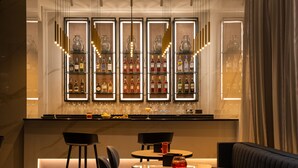 A bar area with multiple shelves of bottles, bar stools, and a seating area with a sofa and round tables. - Savhotel Fiera Bologna (Bologna)