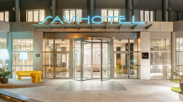 The entrance of a hotel with a revolving door and a neon sign that reads "SANHOTEL".